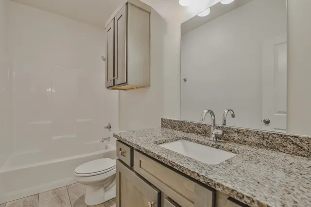 a bathroom with a granite countertop sink a toilet and bathtub