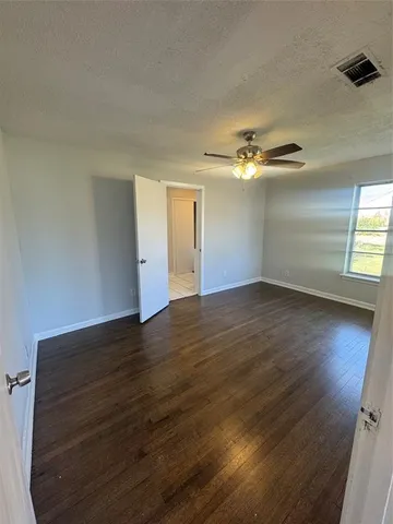 an empty room with wooden floor chandelier fan and windows