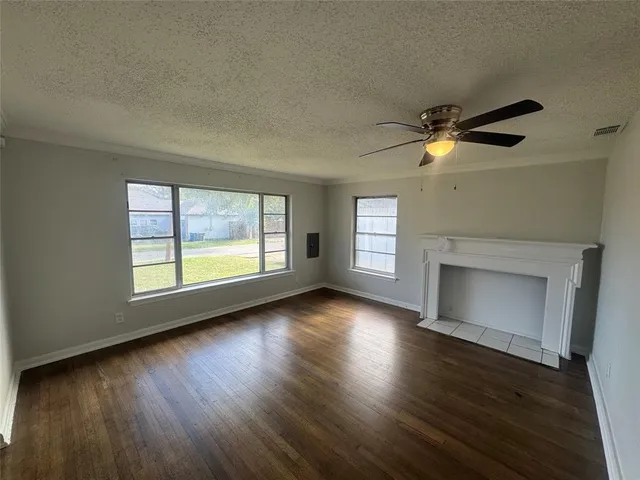 an empty room with wooden floor fireplace and windows