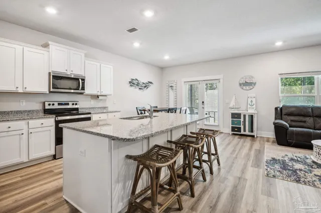 a kitchen with stainless steel appliances kitchen island granite countertop a stove top oven a sink a dining table and chairs with wooden floor
