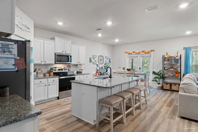 a kitchen with stainless steel appliances kitchen island granite countertop a refrigerator a stove top oven a sink dishwasher and white cabinets with wooden floor