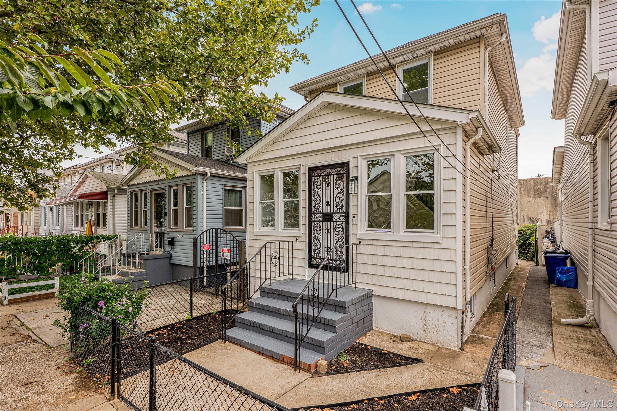 173-43 103rd Road Queens, NY 11433 - Photo 43 of 43 Two-story exterior with light-toned siding, a front porch, and a fenced front yard