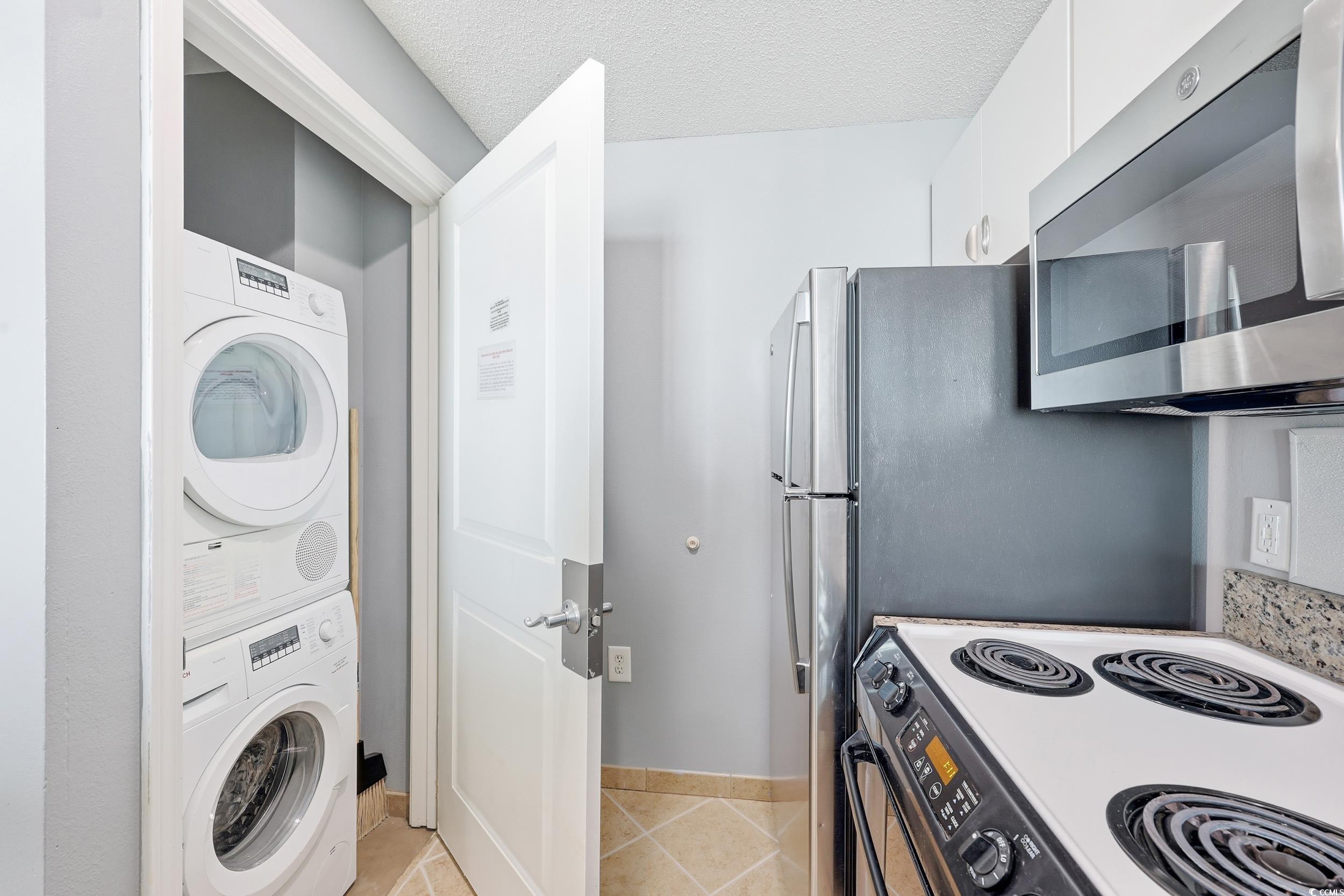 300 North Ocean Boulevard, Unit 1608 North Myrtle Beach, SC 29582 - Photo 15 of 30 Kitchen featuring electric stove, stainless steel microwave, light tile patterned floors, stacked washer / dryer, and white cabinetry