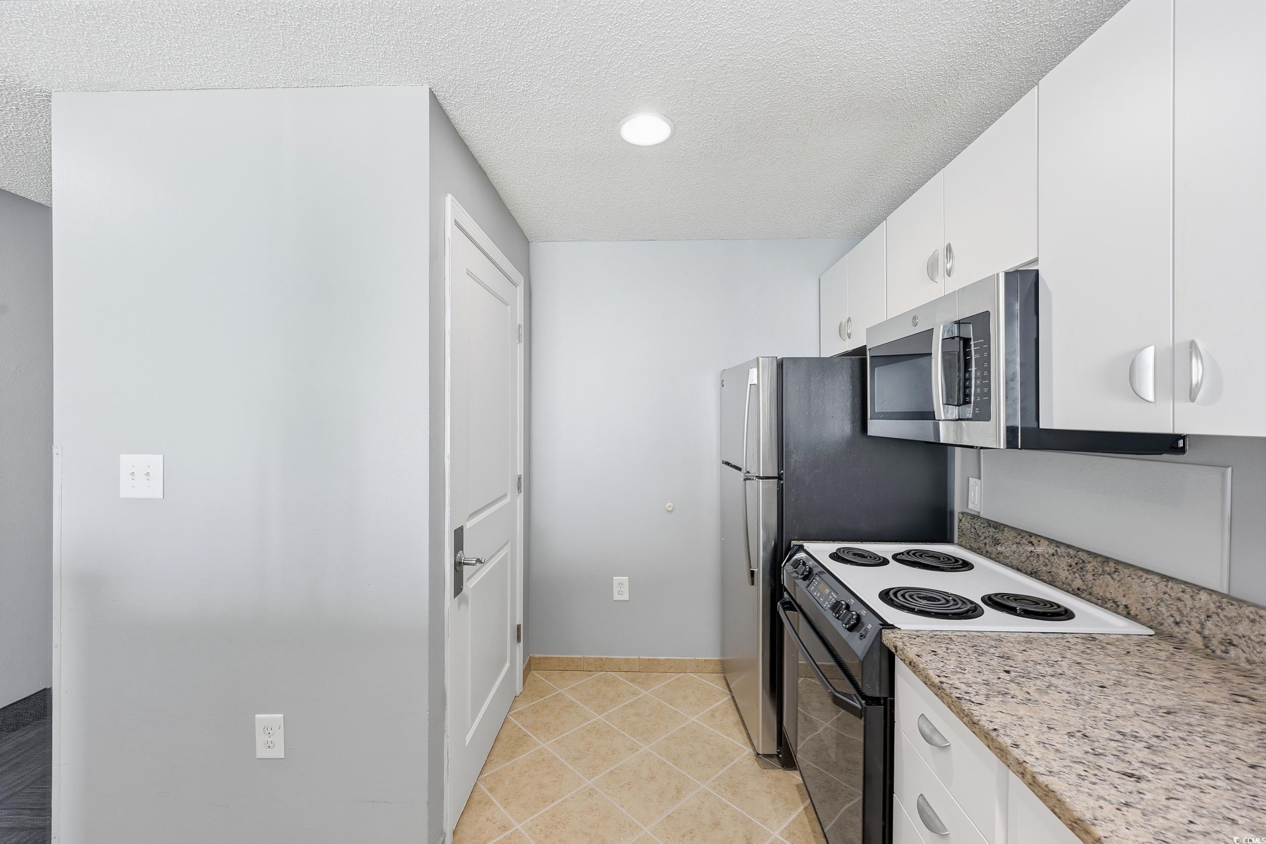 300 North Ocean Boulevard, Unit 1608 North Myrtle Beach, SC 29582 - Photo 2 of 30 Kitchen featuring stainless steel appliances, a textured ceiling, white cabinets, light tile patterned floors, and light stone countertops