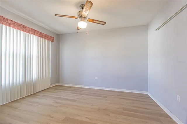 an empty room with wooden floor fan and windows