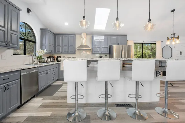 a kitchen with stainless steel appliances kitchen island granite countertop a table chairs in it and white cabinets