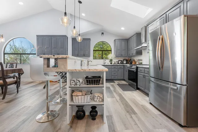 a kitchen with stainless steel appliances granite countertop a refrigerator a stove a sink dishwasher a dining table and chairs with wooden floor