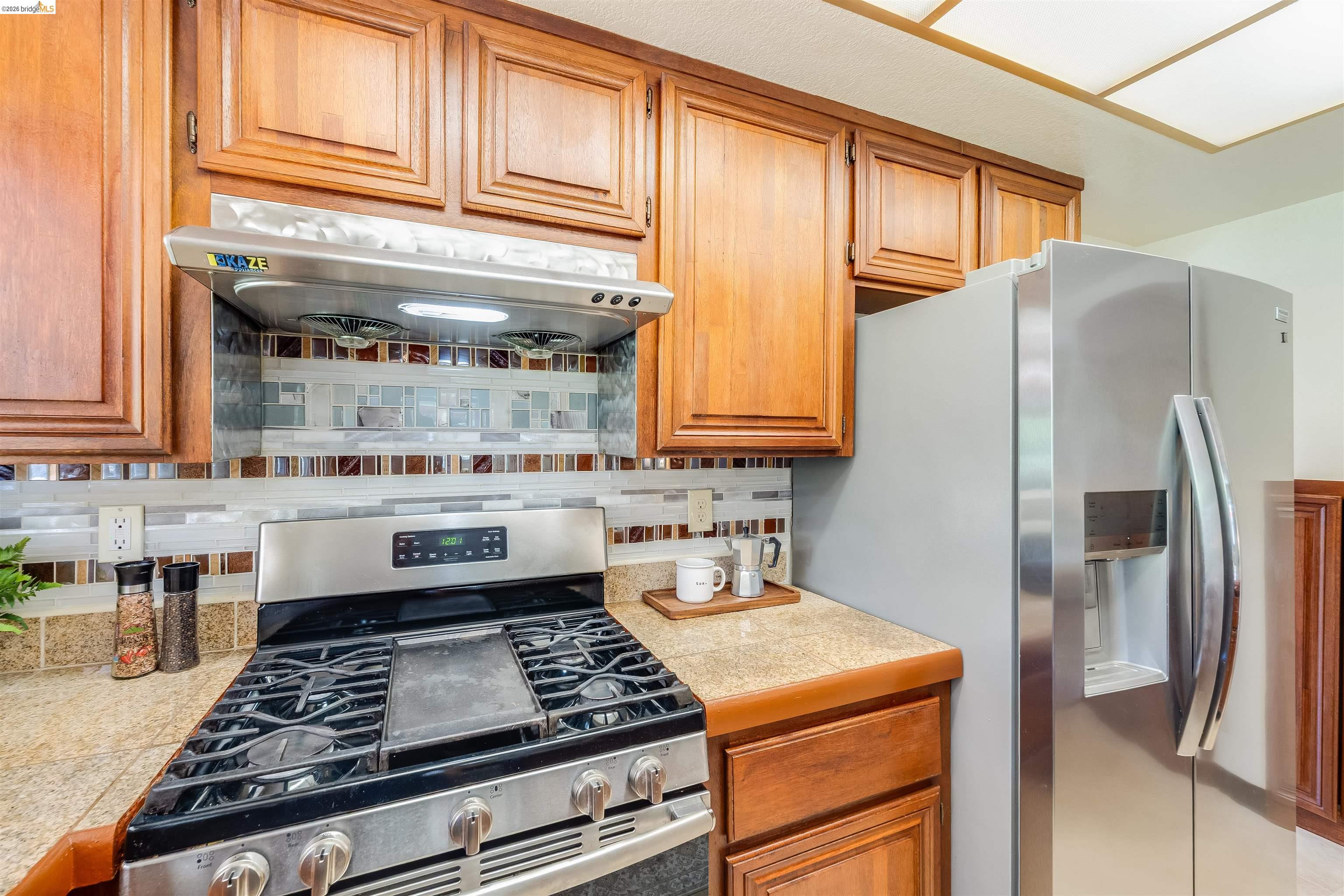2142 Redwood Road Hercules, CA 94547 - Photo 12 of 37 Kitchen featuring stainless steel appliances, backsplash, wood finish cabinetry, and tile counters