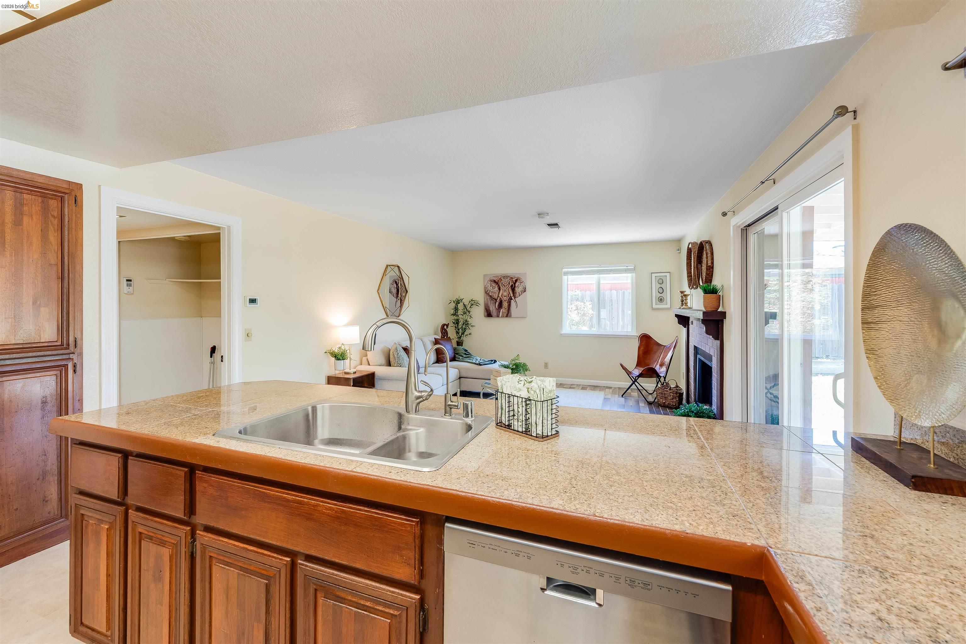 2142 Redwood Road Hercules, CA 94547 - Photo 37 of 37 Kitchen featuring tile counters, stainless steel dishwasher, wood finish cabinetry, open floor plan, and a fireplace