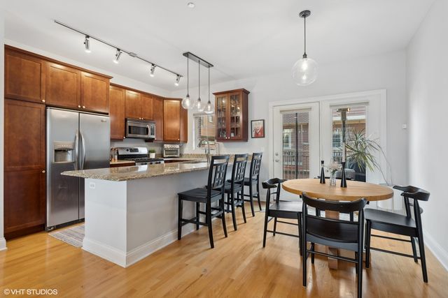 a kitchen with stainless steel appliances kitchen island granite countertop a dining table chairs and a refrigerator
