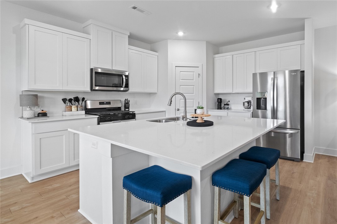 2105 Oliver Street Pea Ridge, AR 72751 - Photo 7 of 26 Modern kitchen featuring an expansive island with seating, white shaker cabinetry, stainless steel appliances, light wood-finish flooring, and recessed lighting