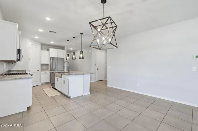 a kitchen with kitchen island granite countertop white cabinets stainless steel appliances and a chandelier