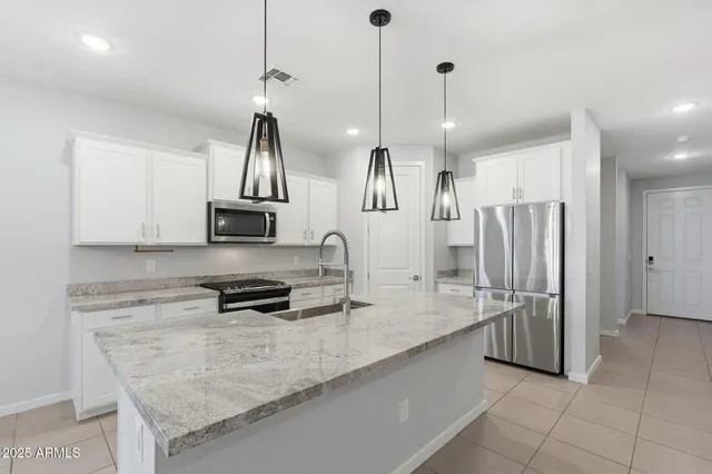 a kitchen with stainless steel appliances granite countertop a sink a stove a refrigerator and white cabinets