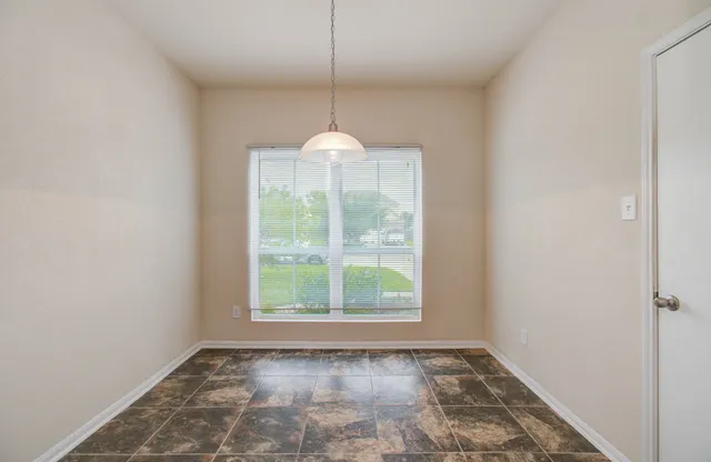 an empty room with kitchen view and a chandelier fan