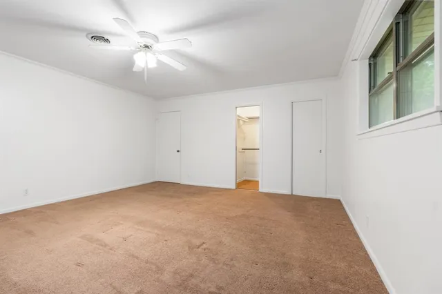an empty room with chandelier fan and windows