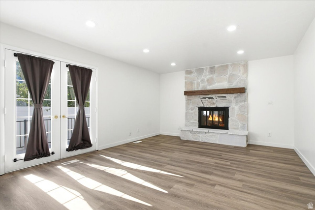 1676 East 11245 South Sandy, UT 84092 - Photo 5 of 34 Living area featuring a stone-clad fireplace with a wood mantel, dual French doors with clear glass panes, light wood-finish flooring, recessed lighting, and white walls