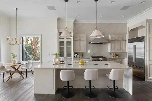 a kitchen with stainless steel appliances granite countertop a stove a refrigerator a kitchen island a dining table and chairs with wooden floor