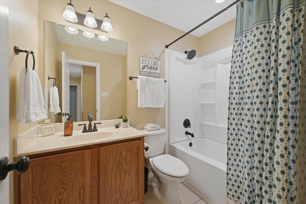 112 Springfield Lane Red Oak, TX 75165 - Photo 24 of 40 Full guest bathroom featuring a wood-finish vanity with a light-toned countertop, an undermount sink, and a three-light vanity fixture