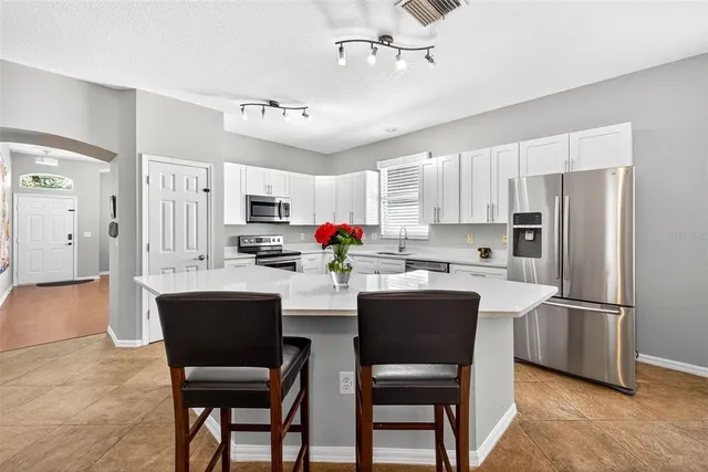 a kitchen with stainless steel appliances kitchen island granite countertop a refrigerator a sink dishwasher a dining table and chairs with wooden floor