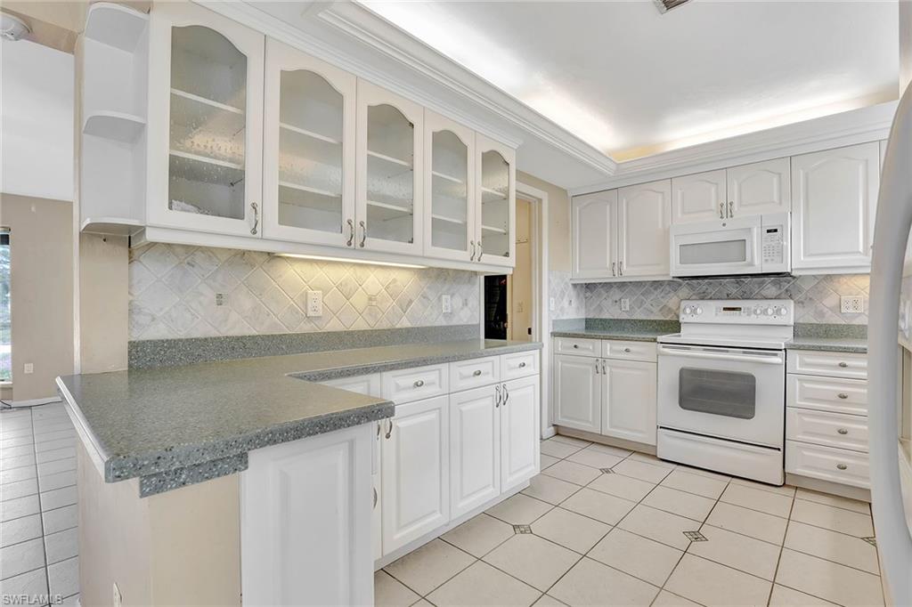 4656 Capri Drive Naples, FL 34103 - Photo 4 of 18 a kitchen with granite countertop white cabinets and white appliances