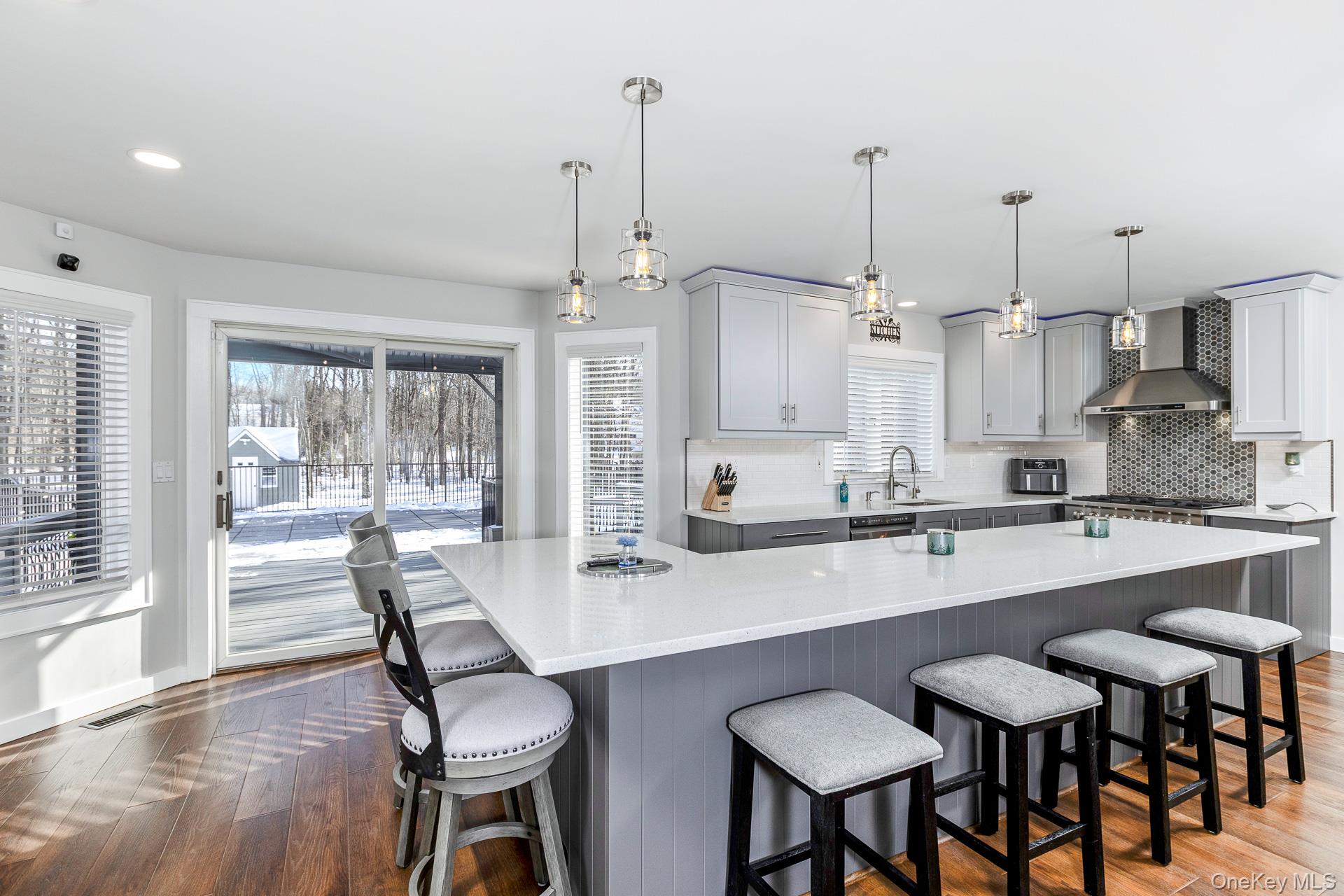 503 Wading River Road Manorville, NY 11949 - Photo 14 of 45 Kitchen with gray cabinets, dark wood-style floors, a kitchen bar, decorative light fixtures, and wall chimney range hood