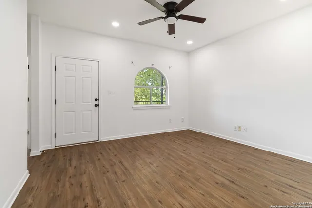 an empty room with wooden floor chandelier fan and windows