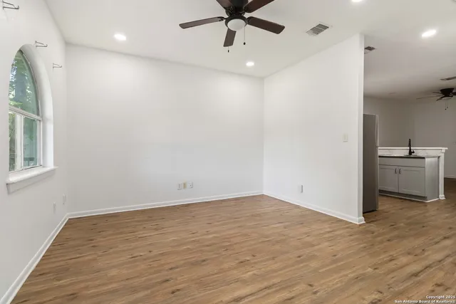 an empty room with wooden floor a ceiling fan and windows