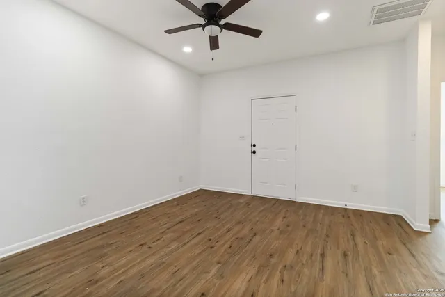 an empty room with wooden floor ceiling fan and windows