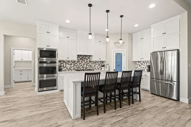a kitchen with stainless steel appliances granite countertop a dining table chairs refrigerator and microwave