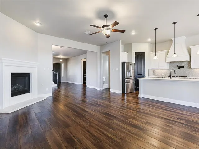 a view of an empty room and kitchen with wooden floor and a ceiling fan