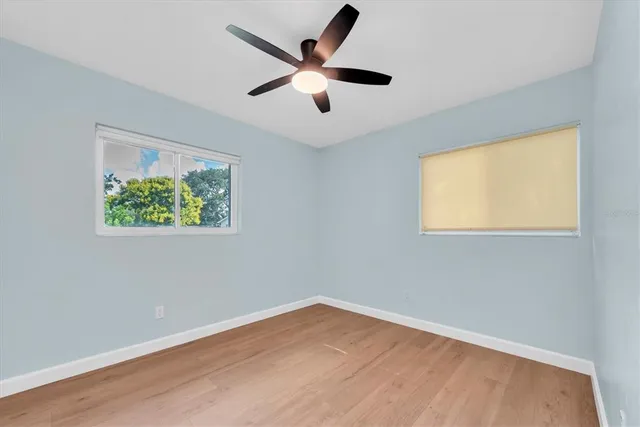 a view of an empty room with wooden floor and a ceiling fan
