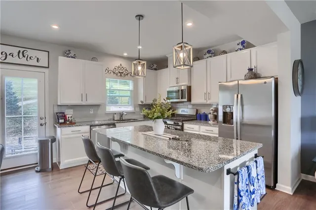 a kitchen with stainless steel appliances granite countertop a sink a stove a refrigerator cabinets and chairs