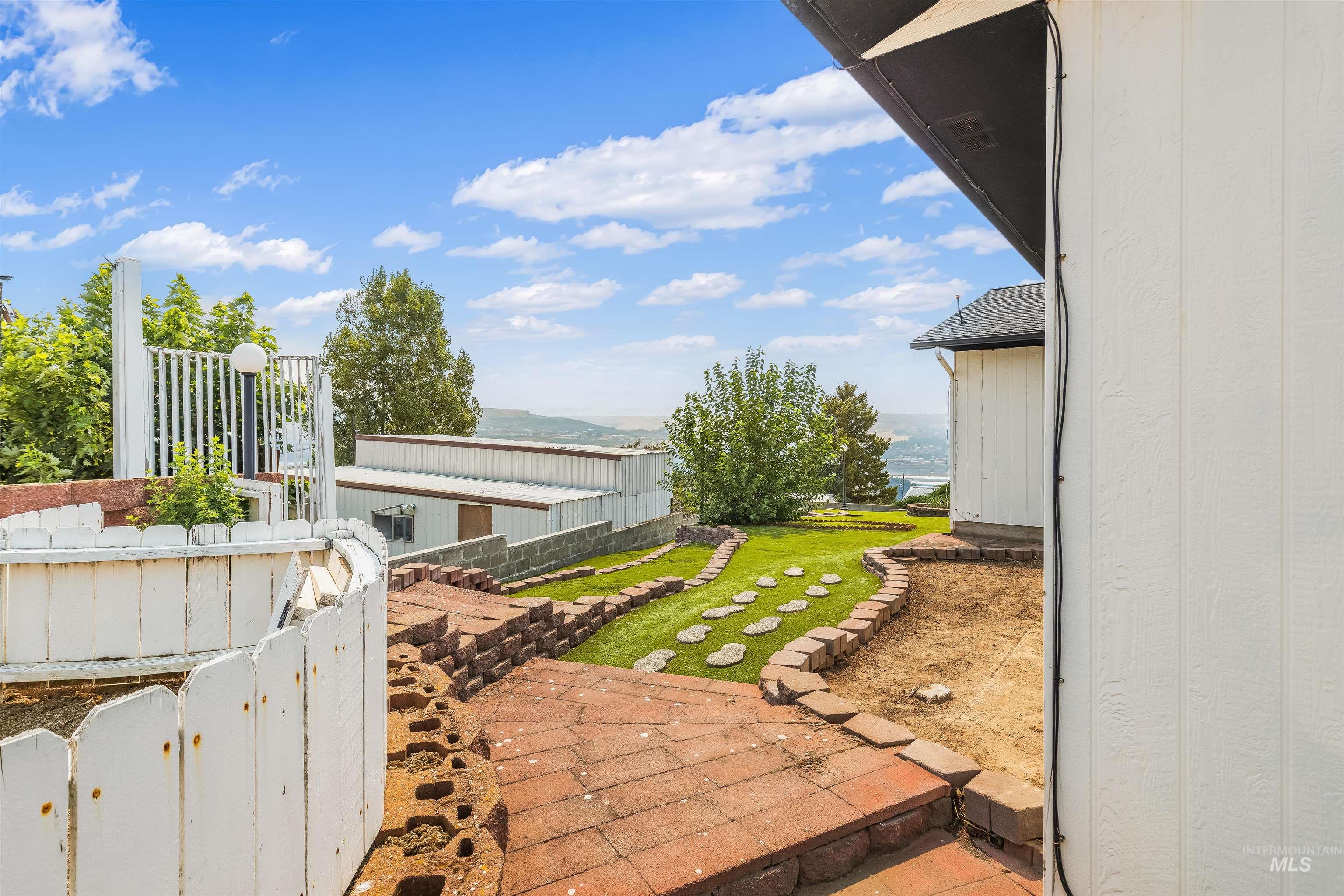1133 Harvest Road Lewiston, ID 83501 - Photo 10 of 45 Tiered backyard featuring brick paver pathways, artificial turf sections with stepping stones, and decorative retaining walls