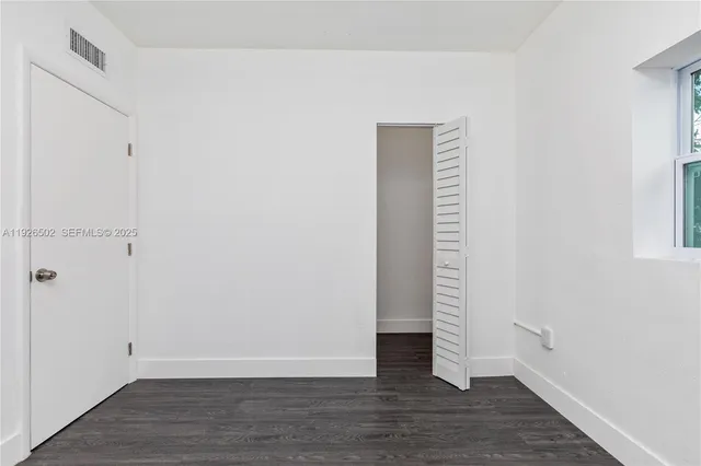 a view of an empty room with wooden floor and a window