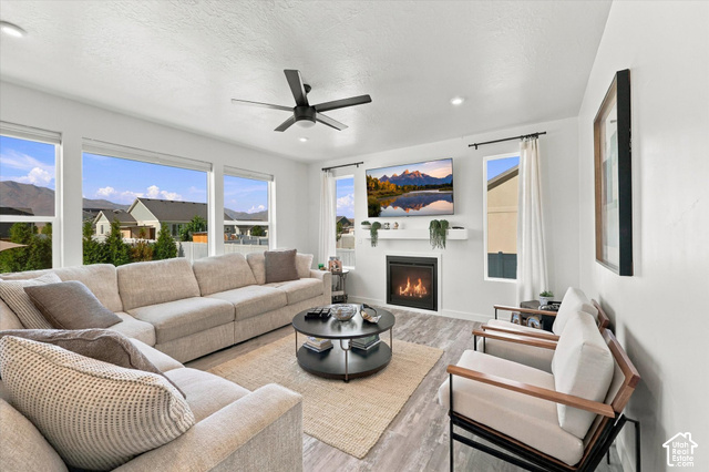 7939 Seattle Slew Road Eagle Mountain, UT 84005 - Photo 10 of 52 Spacious living area featuring abundant natural light, wood-finish flooring, a contemporary ceiling fan, and a built-in fireplace with a mantel