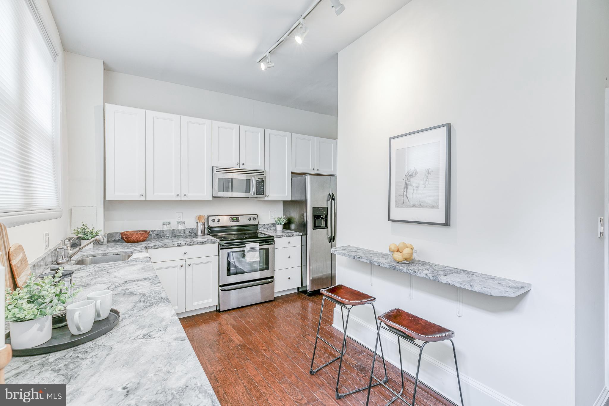 1714 Rittenhouse Square Philadelphia, PA 19103 - Photo 7 of 21 a kitchen with stainless steel appliances granite countertop a stove top oven a sink a dining table and chairs with white cabinets