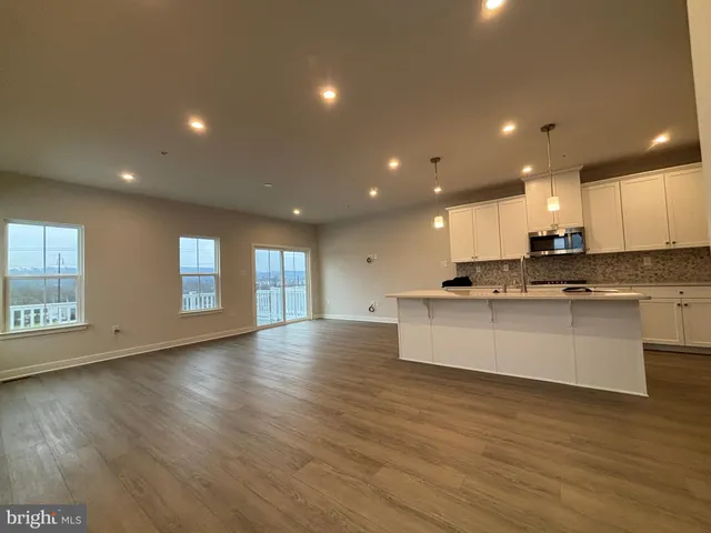 a view of an empty room with wooden floor and kitchen