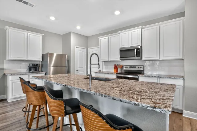 a kitchen with stainless steel appliances granite countertop a stove top oven a sink a refrigerator with white cabinets and wooden floor