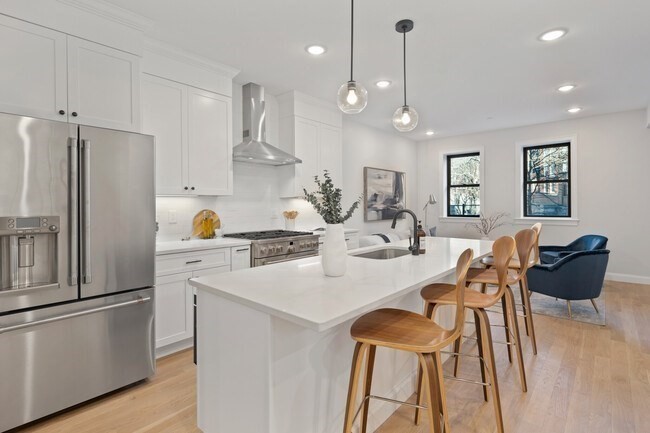a kitchen with stainless steel appliances kitchen island granite countertop a refrigerator a sink dishwasher a dining table and chairs with wooden floor