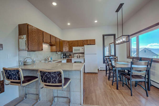 98000 Ryan Gulch Road, Unit E104 Silverthorne, CO 80498 - Photo 7 of 34 a kitchen with kitchen island granite countertop a dining table chairs and white cabinets