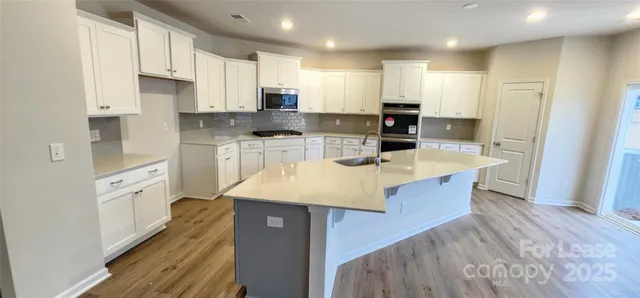 a kitchen with stainless steel appliances kitchen island granite countertop a refrigerator a stove top oven a sink and dishwasher with wooden floor