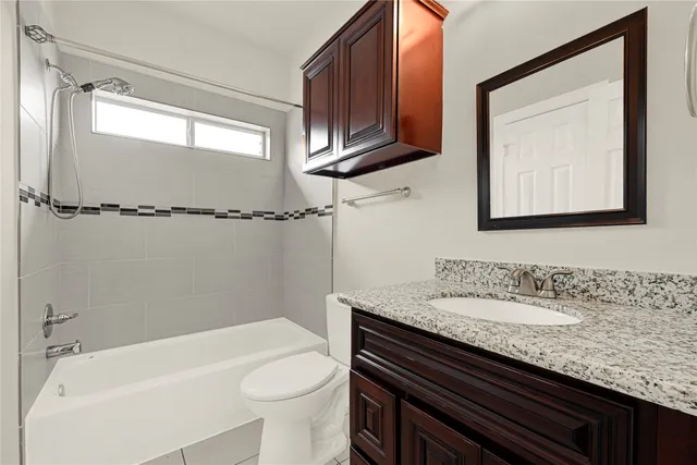 a bathroom with a granite countertop sink a toilet a mirror and bathtub