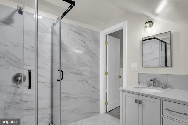 a bathroom with a granite countertop sink a mirror a glass door and shower