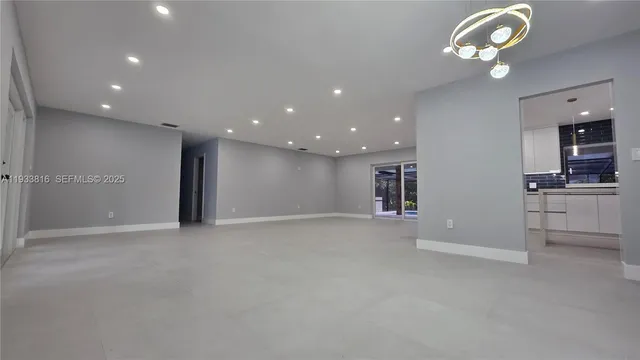 an empty room with a kitchen and chandelier fan