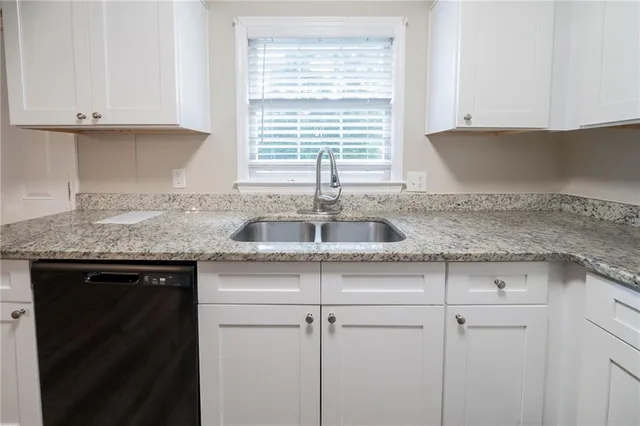 a kitchen with granite countertop a sink white cabinets and a window