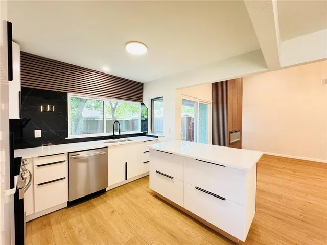 a large kitchen with granite countertop a sink and white cabinets with wooden floor