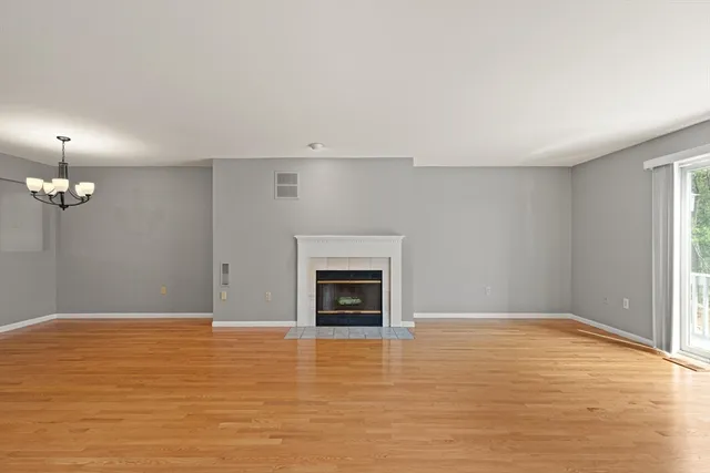 an empty room with wooden floor fireplace and window