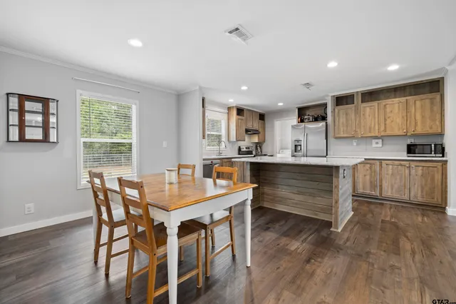 a kitchen with stainless steel appliances kitchen island granite countertop a table chairs sink refrigerator and cabinets