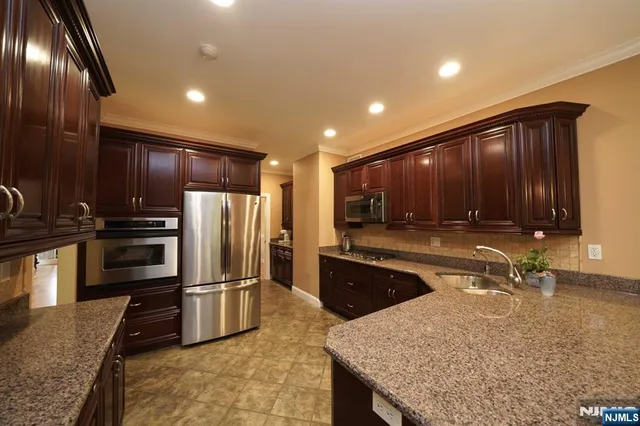 a kitchen with stainless steel appliances granite countertop a refrigerator a stove and a sink with wooden cabinets