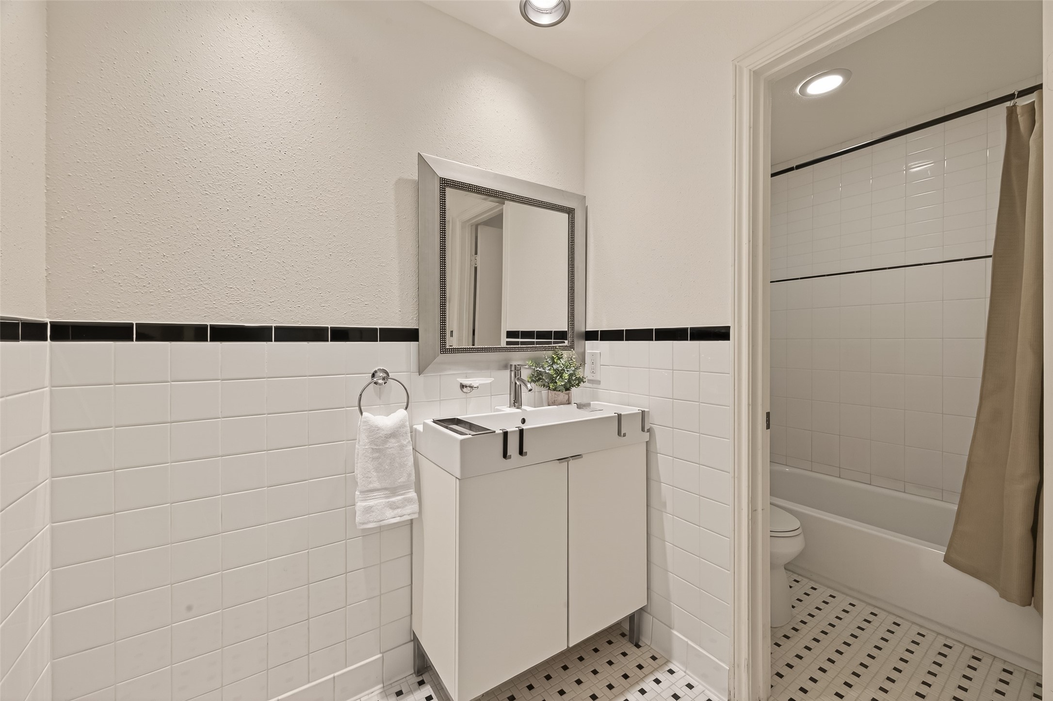 2829 Timmons Lane, Unit 144 Houston, TX 77027 - Photo 19 of 41 This bathroom features a clean, modern design with white tiled walls and black accents. The space is well-lit and has a patterned tile floor for added style.